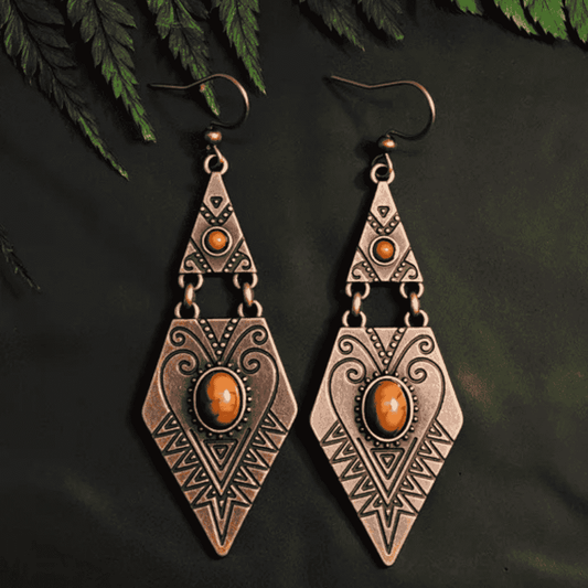 Pair of bronze-colored earrings with orange gemstones on a dark background