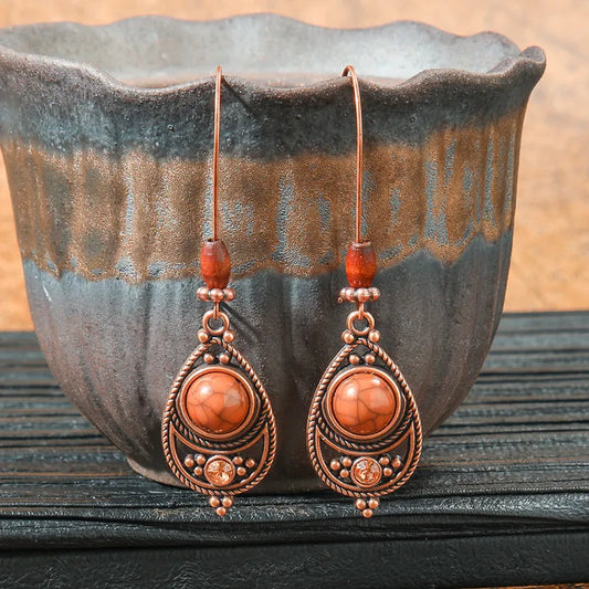 Pair of ornate earrings with orange beads against a rustic background