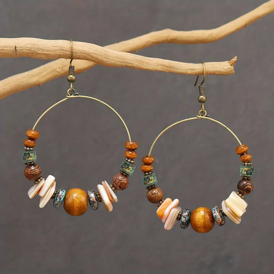 Hoop earrings with bead and shell decorations on a branch against a gray background