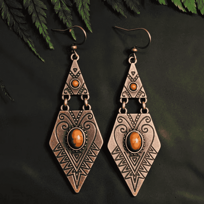 Pair of bronze-colored earrings with orange gemstones on a dark background