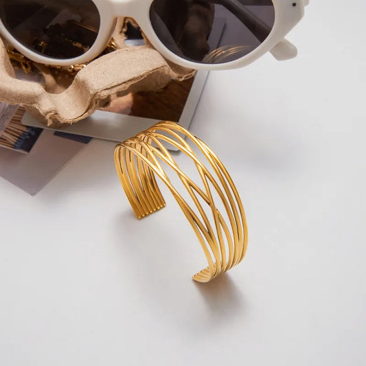 Gold cuff bracelet on a white surface with sunglasses in the background