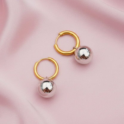 Gold hoop earrings with silver spherical charms on a pink fabric background